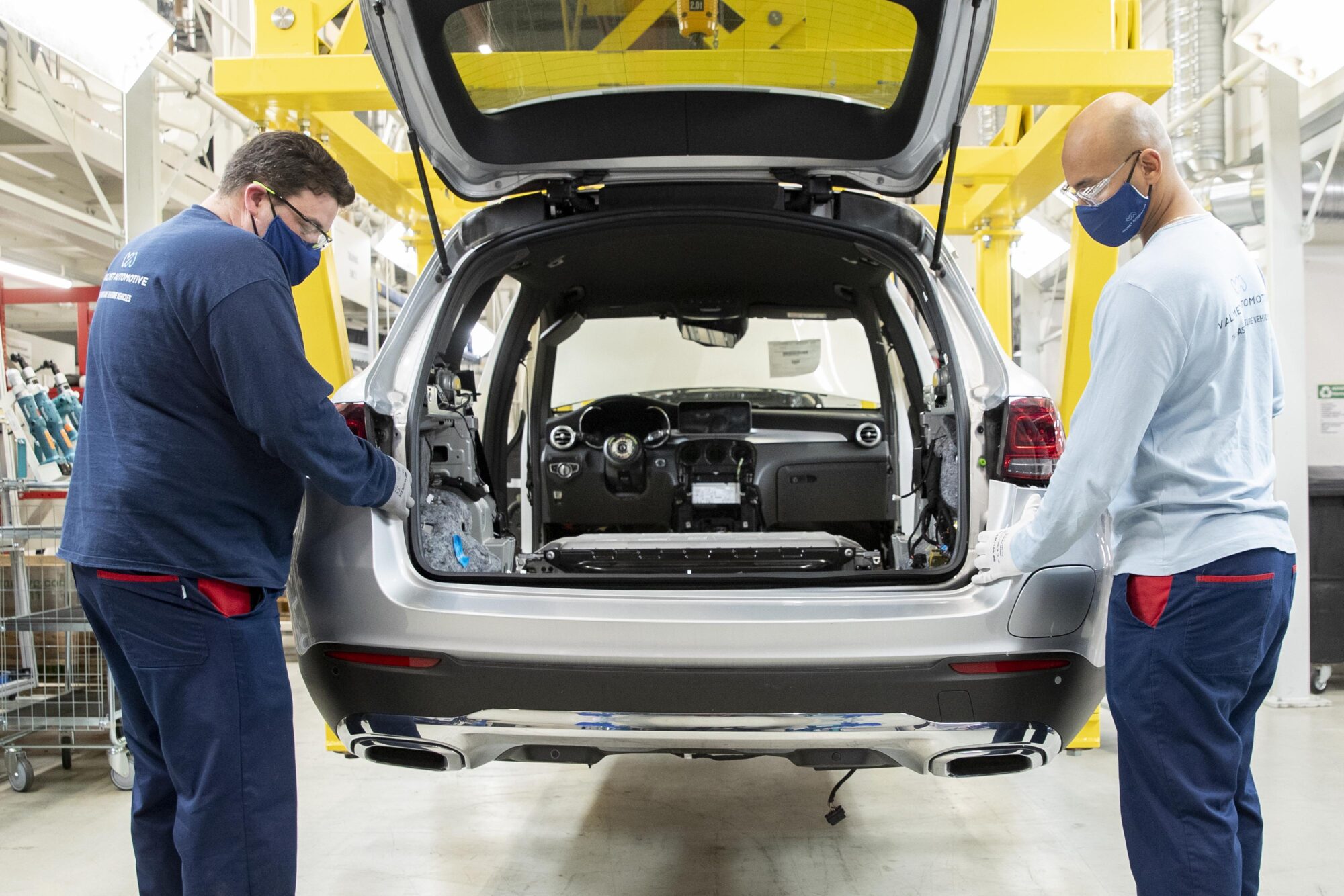 Kaksi miestä työskentelee auton korin ääressä autotehtaalla