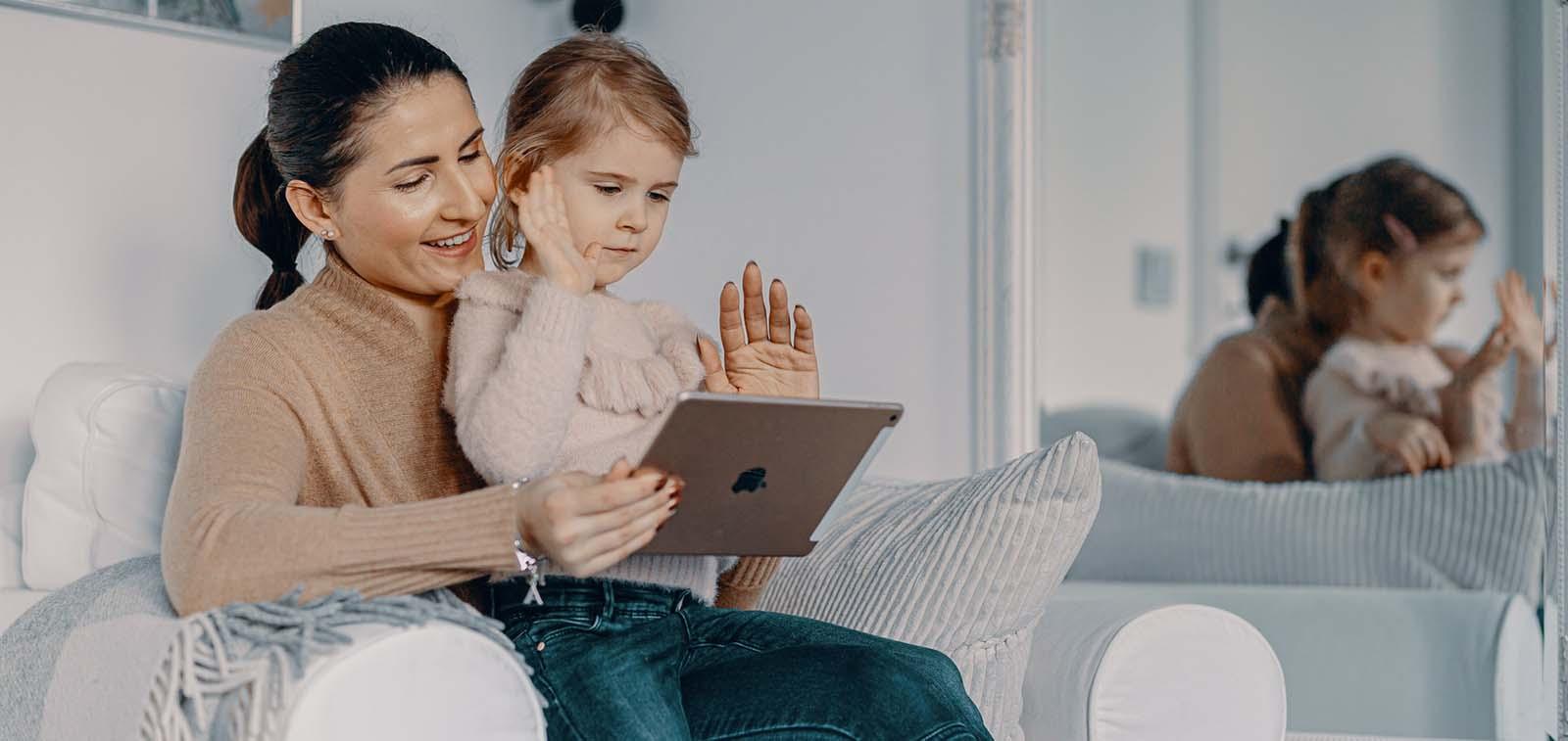 Lapsi istuu äidin sydlissä katsomassa tabletilta jotakin