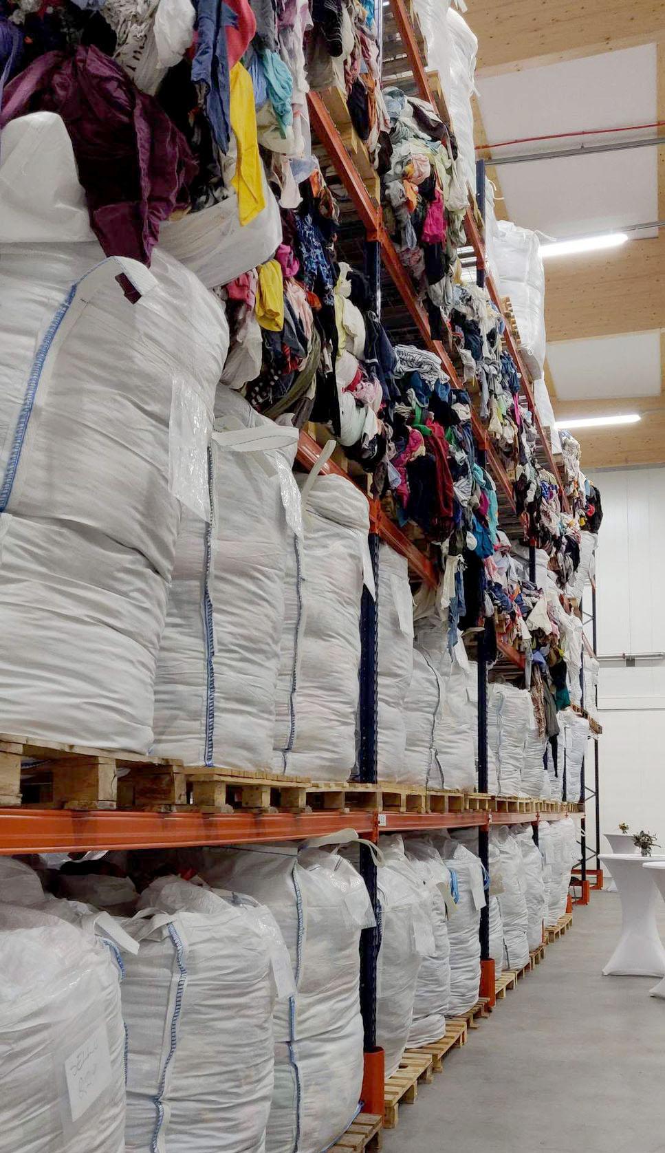 Poistotekstiilejä säkeissä ja hyllyillä pinottuna poistotekstiilien kiertotalouslaitoksen varastossa.