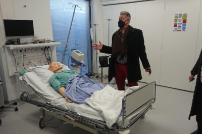 Mies seisoo sairaalsängyn vieressä. Sängyssä makaa potilasta esittävä nukke.