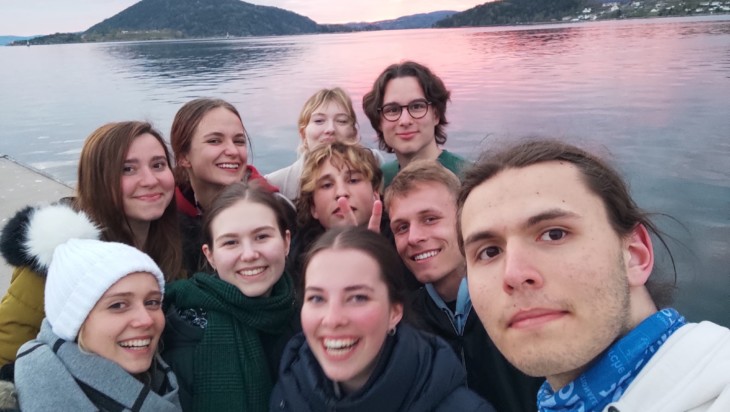 Joukko nuoria poseeraa selfiessä merimaiseman äärellä auringonlaskun aikaan