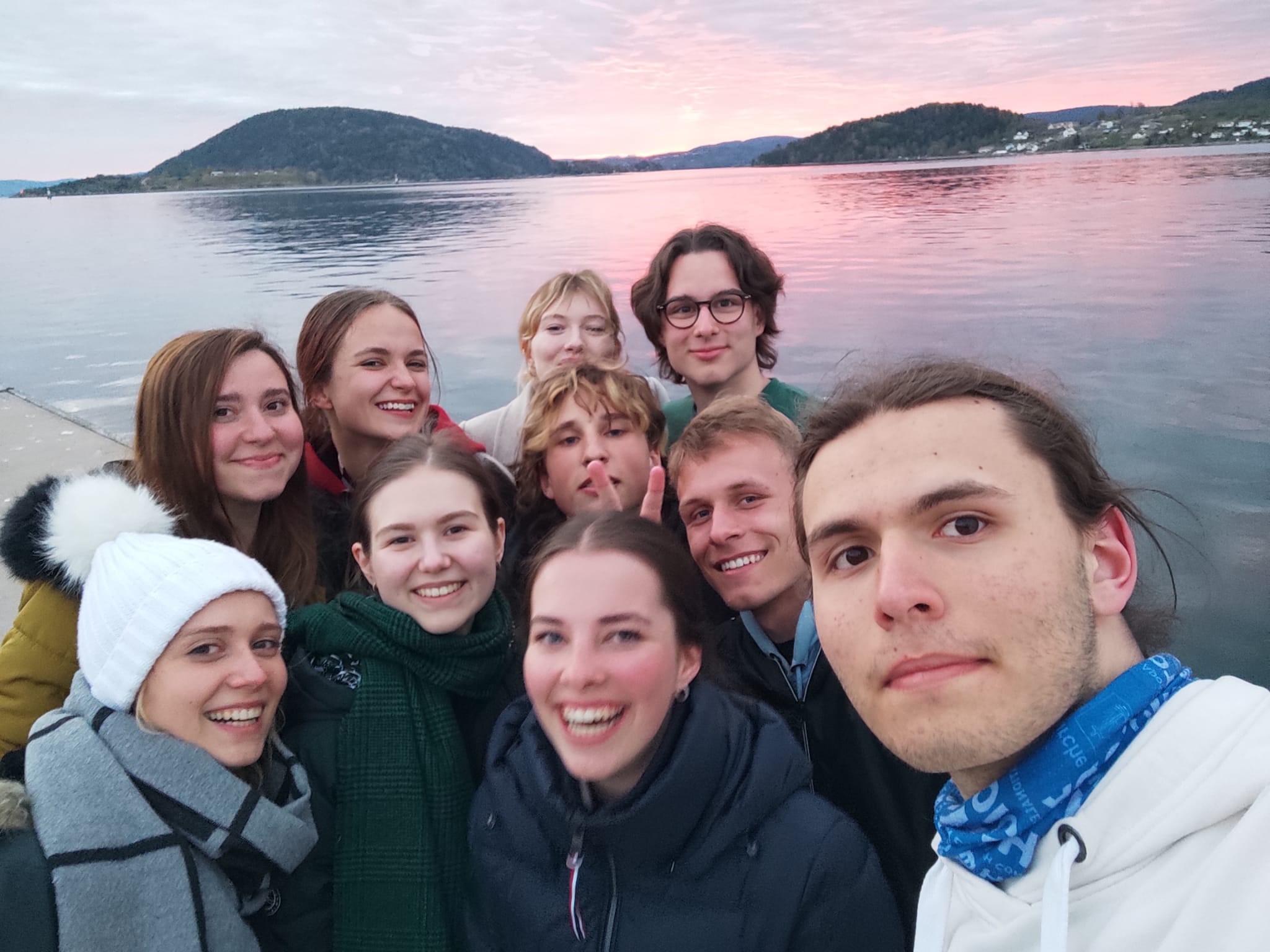 Joukko nuoria poseeraa selfiessä merimaiseman äärellä auringonlaskun aikaan