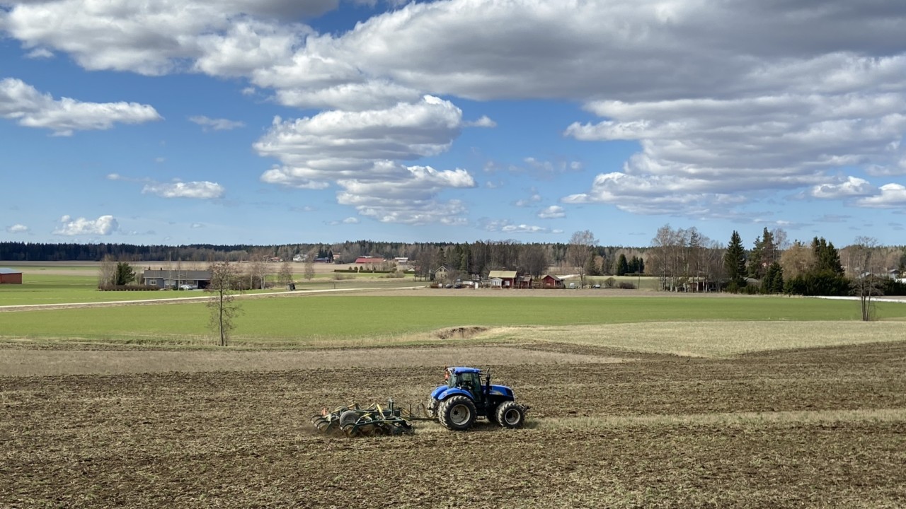 Peltomaisema pilvipoutaisena päivänä, traktor pellonmuokkaustöissä. i