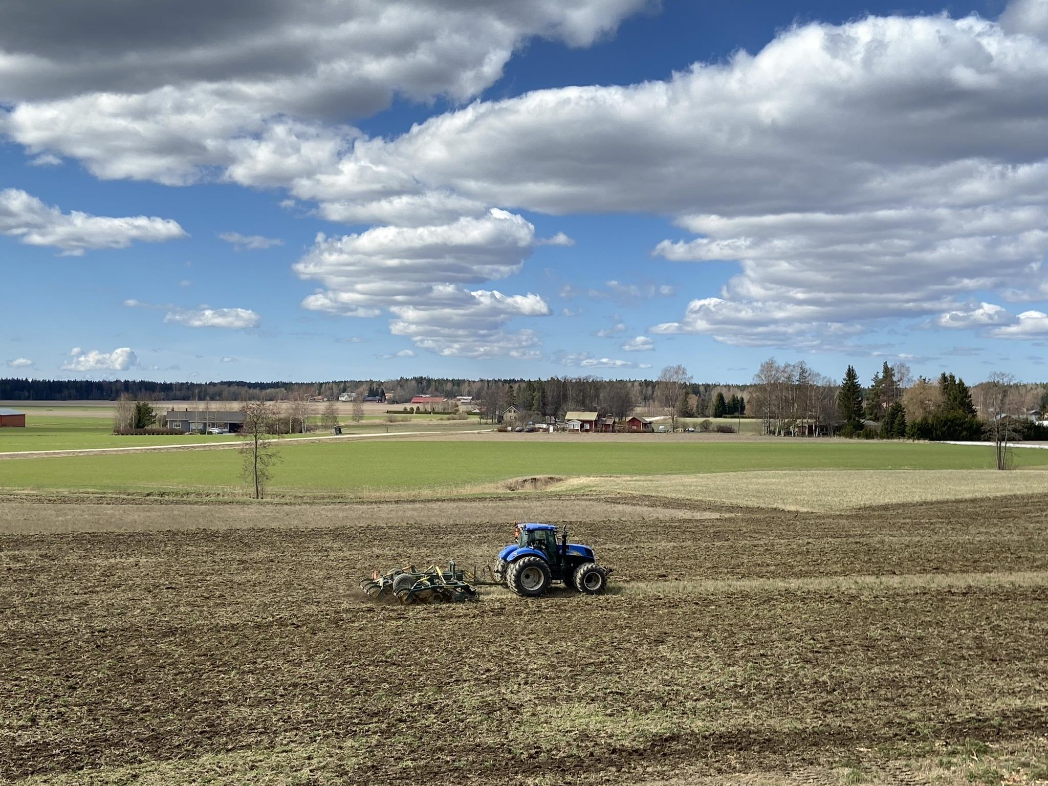 Peltomaisema pilvipoutaisena päivänä, traktor pellonmuokkaustöissä. i