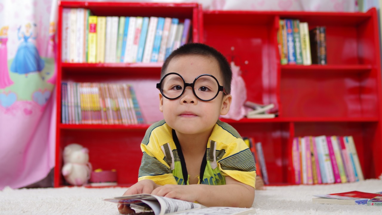 Pieni poika, jolla on isot silmälasit, lukee kirjaa