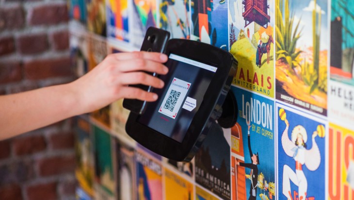 Käyttäjä skannaa näytöltä QR-koodia kännykällään.