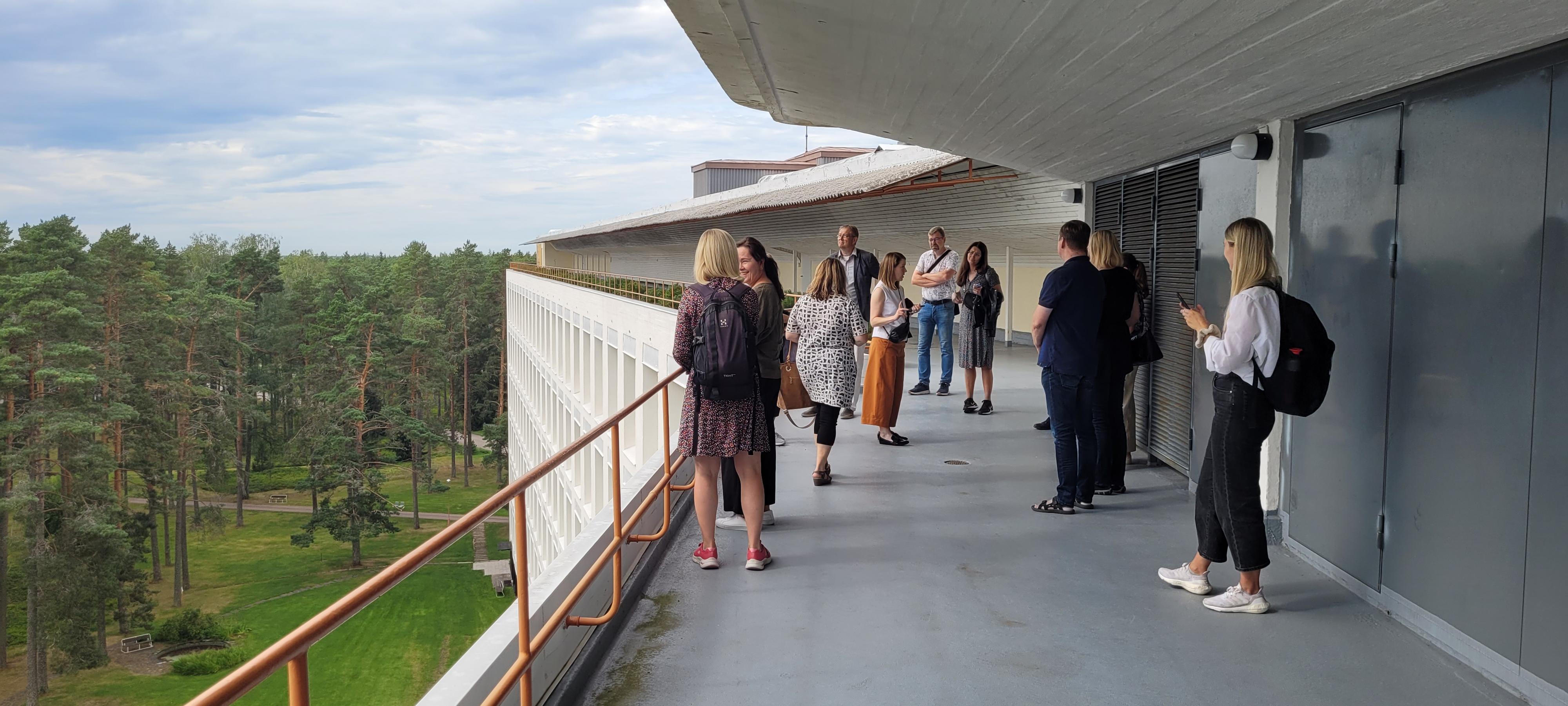 Ihmisiä katselee mäntymetsää rakennuksen parvekkeelta