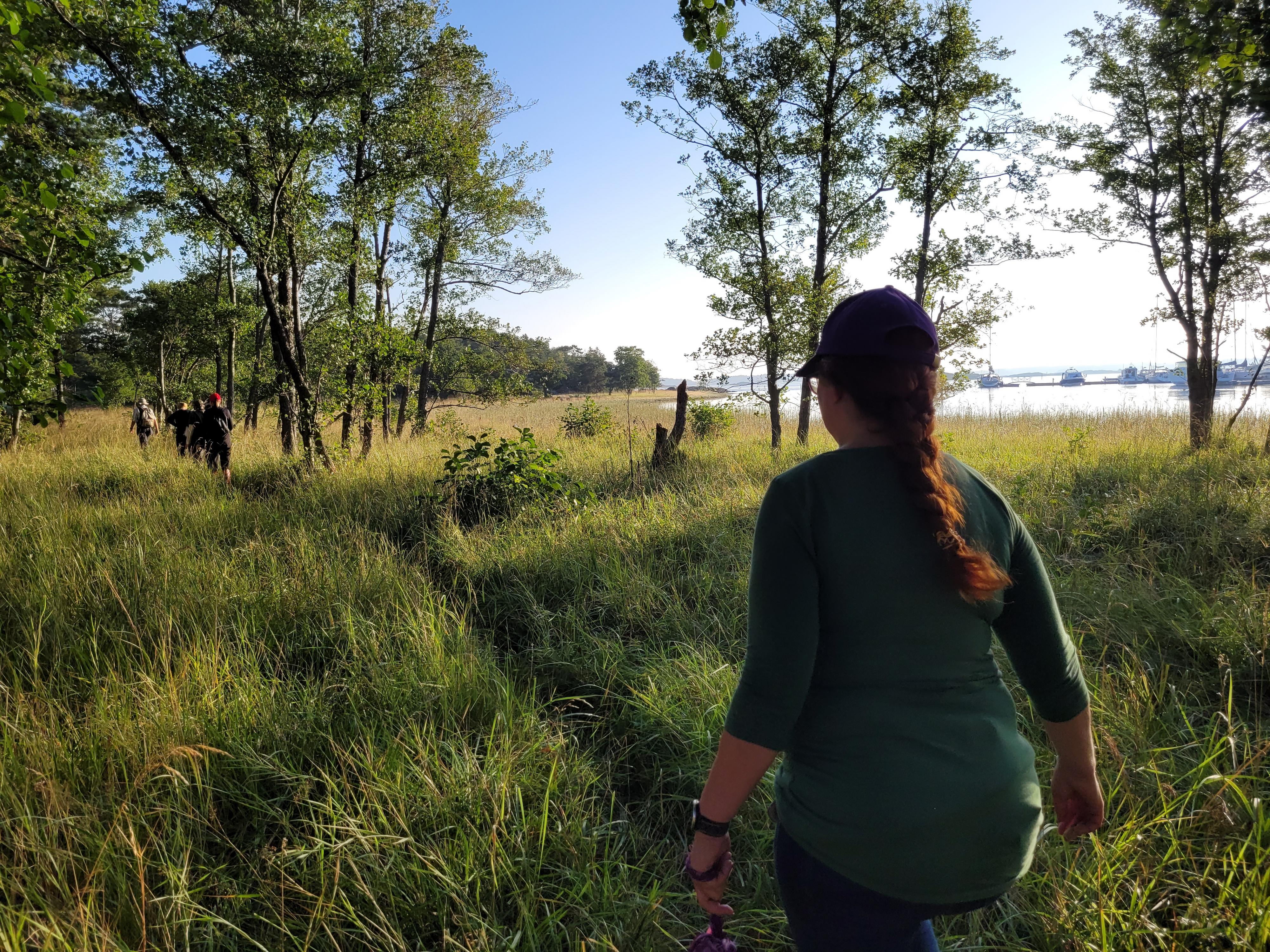 Ihmisiä kävelee rantaniityn polulla aamuauringossa.