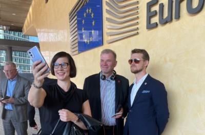 Nainen ja kaksi miestä ottavat kännykällä selfiekuvaa Euroopan parlamentin päärakennuksen edustalla.