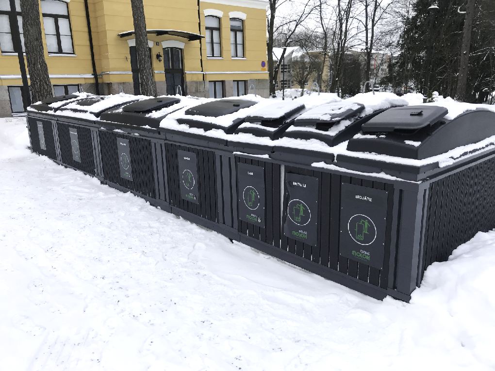 Talvisella kerrostalon pihalla mustia jäteastioita, joissa 7 eri jaetta.