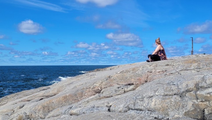 Nainen istuu kalliolla ja katselee merelle