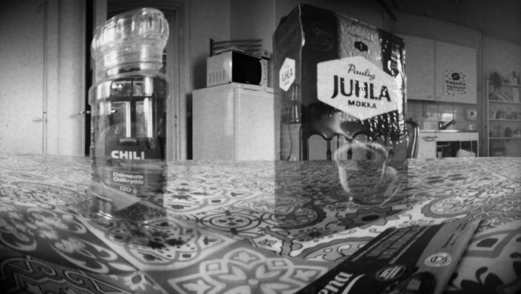 Camera obscura -tekniikalla otettu mustavalkoinen kuva. Kuvassa näkyy taustalla keittiö, etualalla liinalla peitetyllä pöydällä mm. Juhalmokka-paketti..