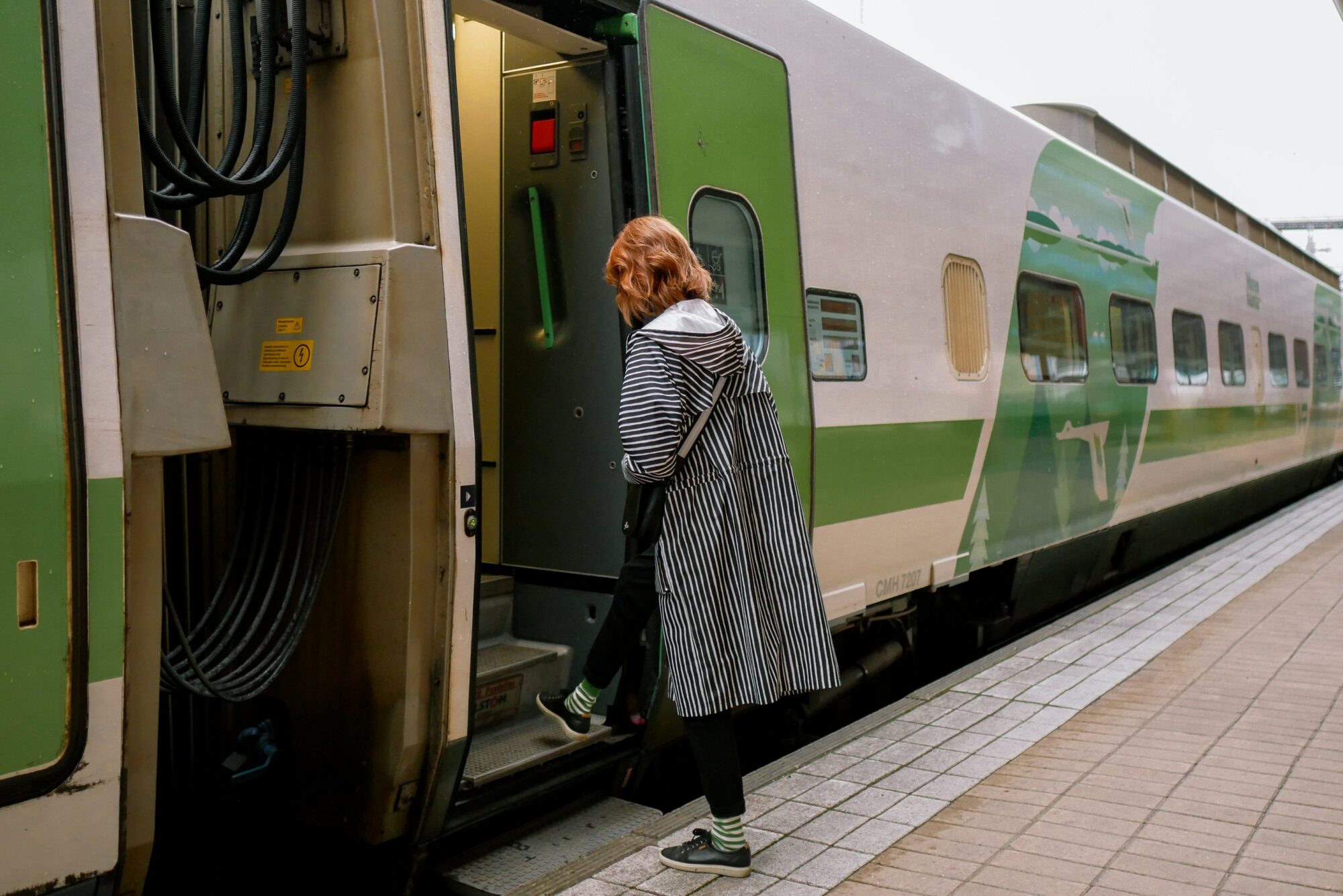 Nainen nousemassa junan kyytiin asemalla