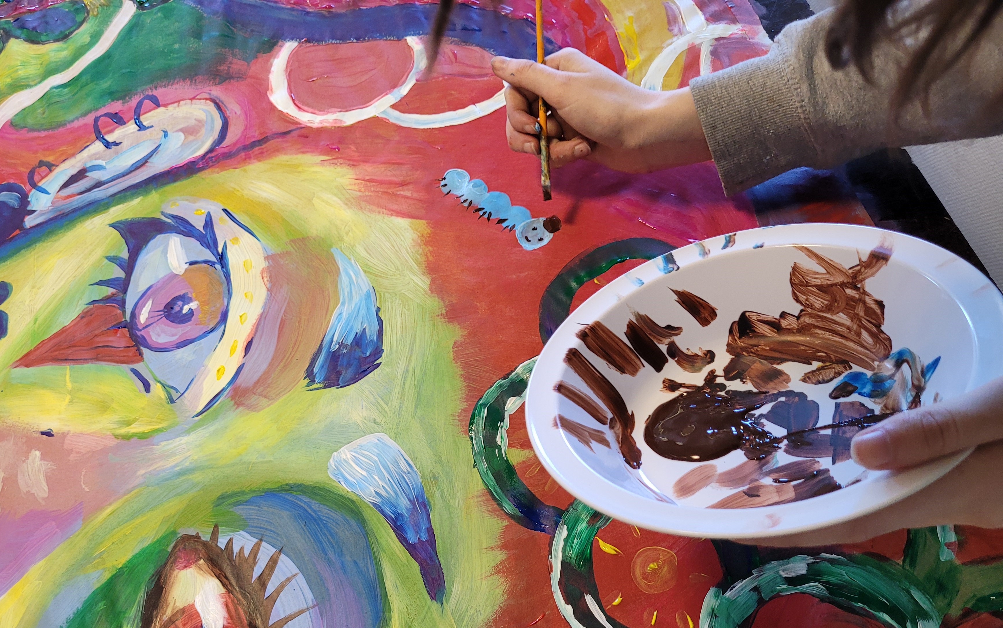 Kuvassa näkyy maalauksen yllä sivellintä pitelevä käsi