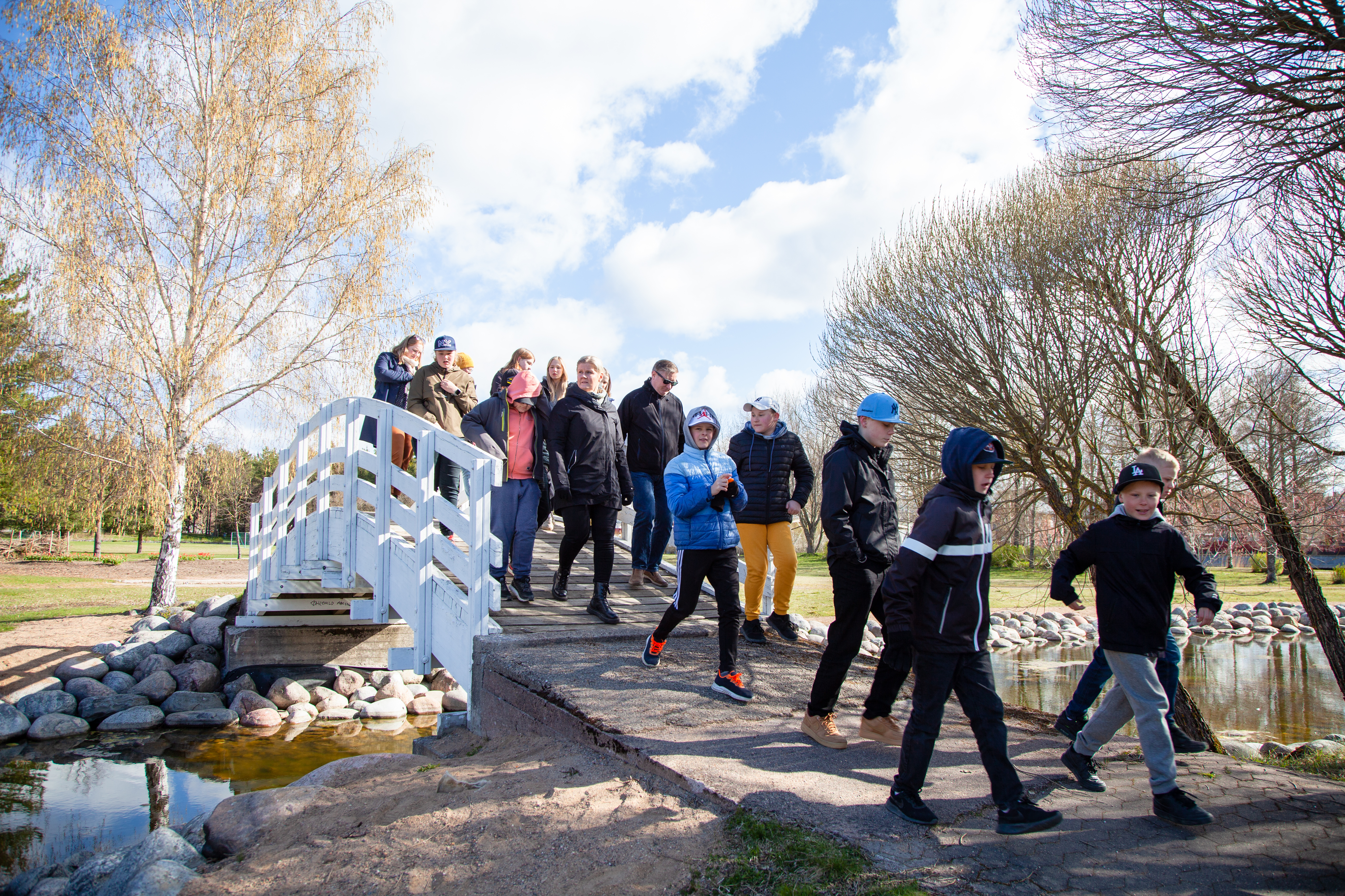 Joukko nuoria kävelemässä valkoisen kävelysillan yli poutapilvisenä päivänä.