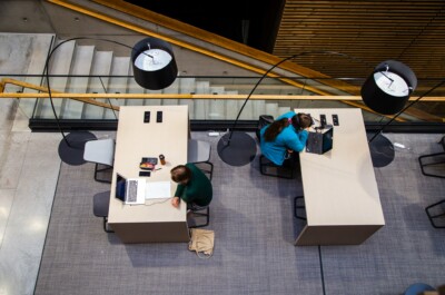 Kaksi opiskelijaa istuu työpöytien ääressä lukemassa.