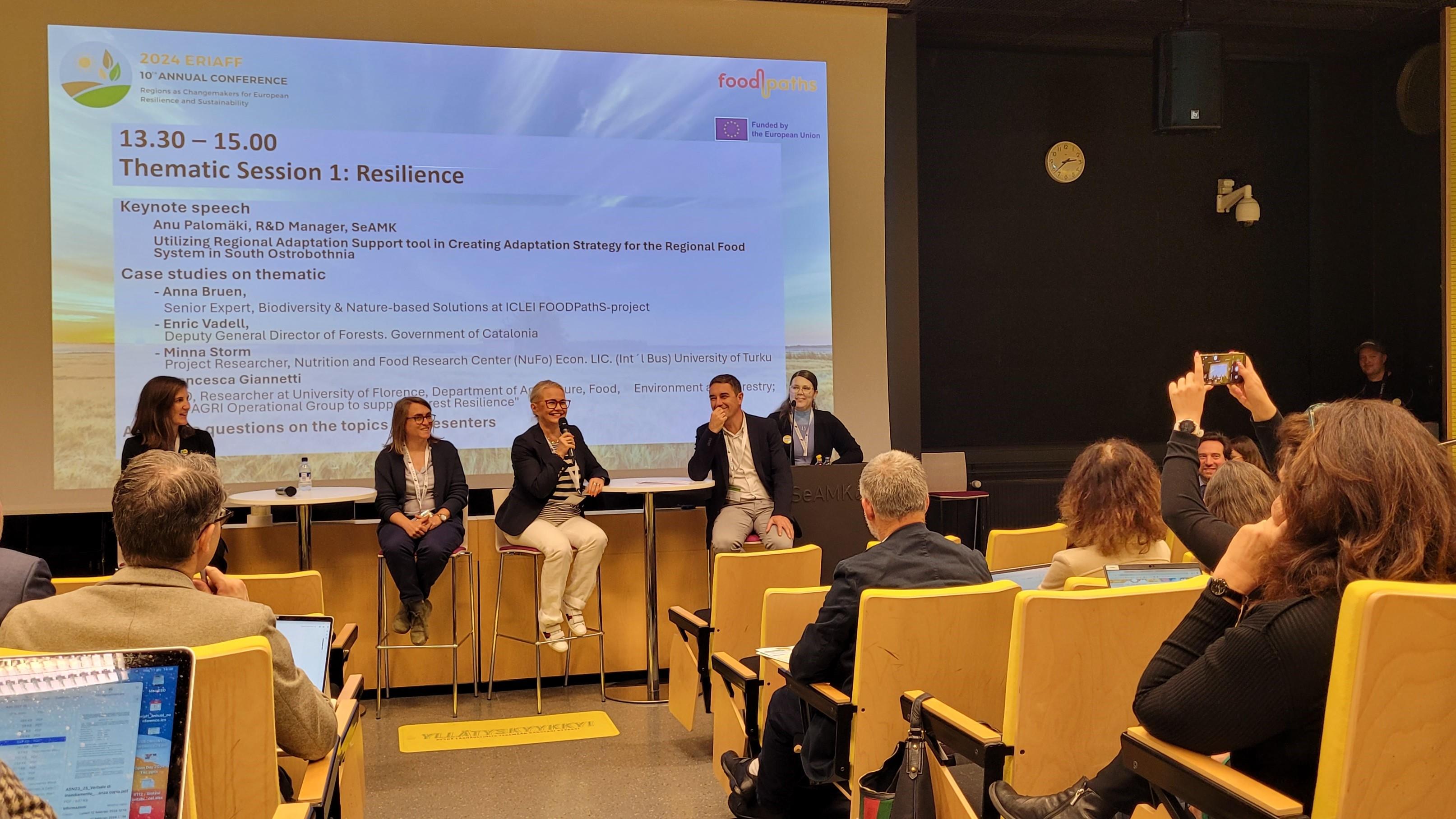 Neljä henkilöä seminaaritilan edessä paneelikeskustelussa ERIAFF-konferenssissa.