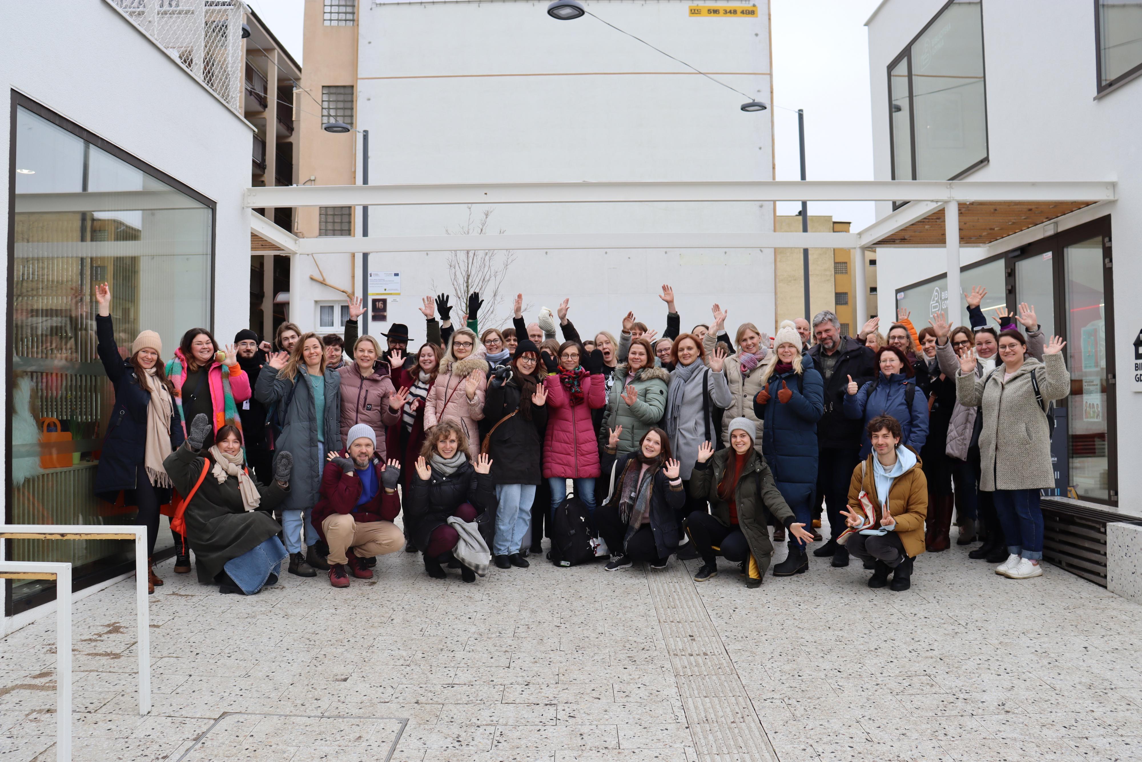 Noin kolmekymmentä ihmistä ryhmäkuvassa ulkona kiveyksellä.