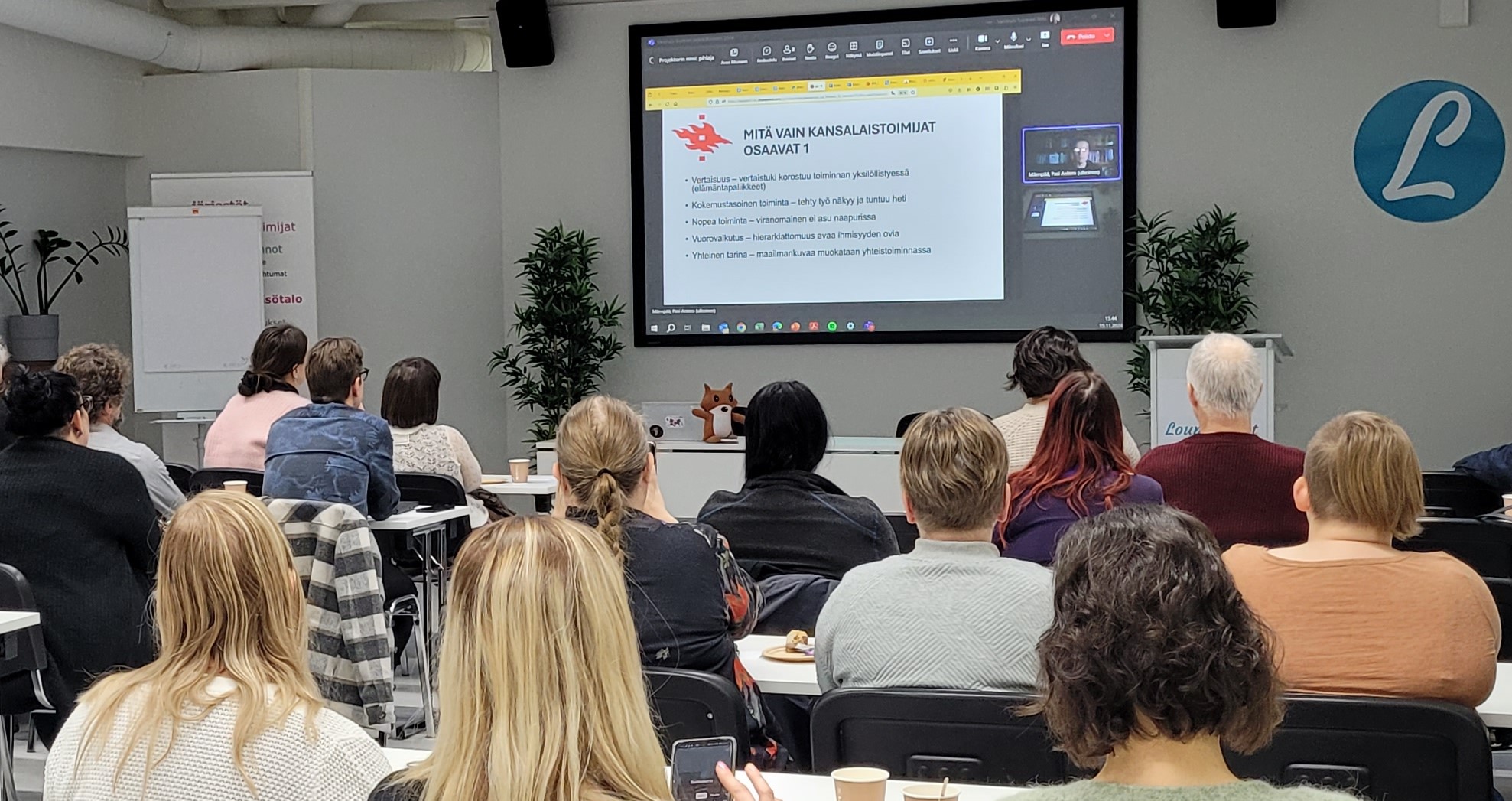 Ihmiset kuuntelevat salissa esitystä kansalaistoimijoiden merkityksestä.