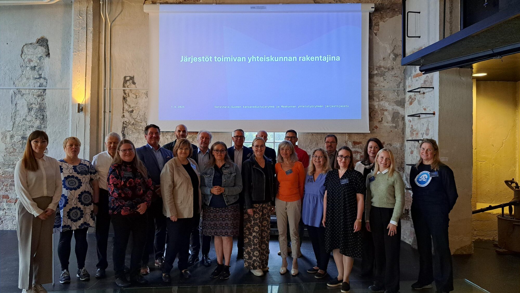 Ryhmäkuva kansanedustajatapaamisen osallistujista Järjestöt toimivan yhteiskunnan rakentajina -diaesityksen edessä