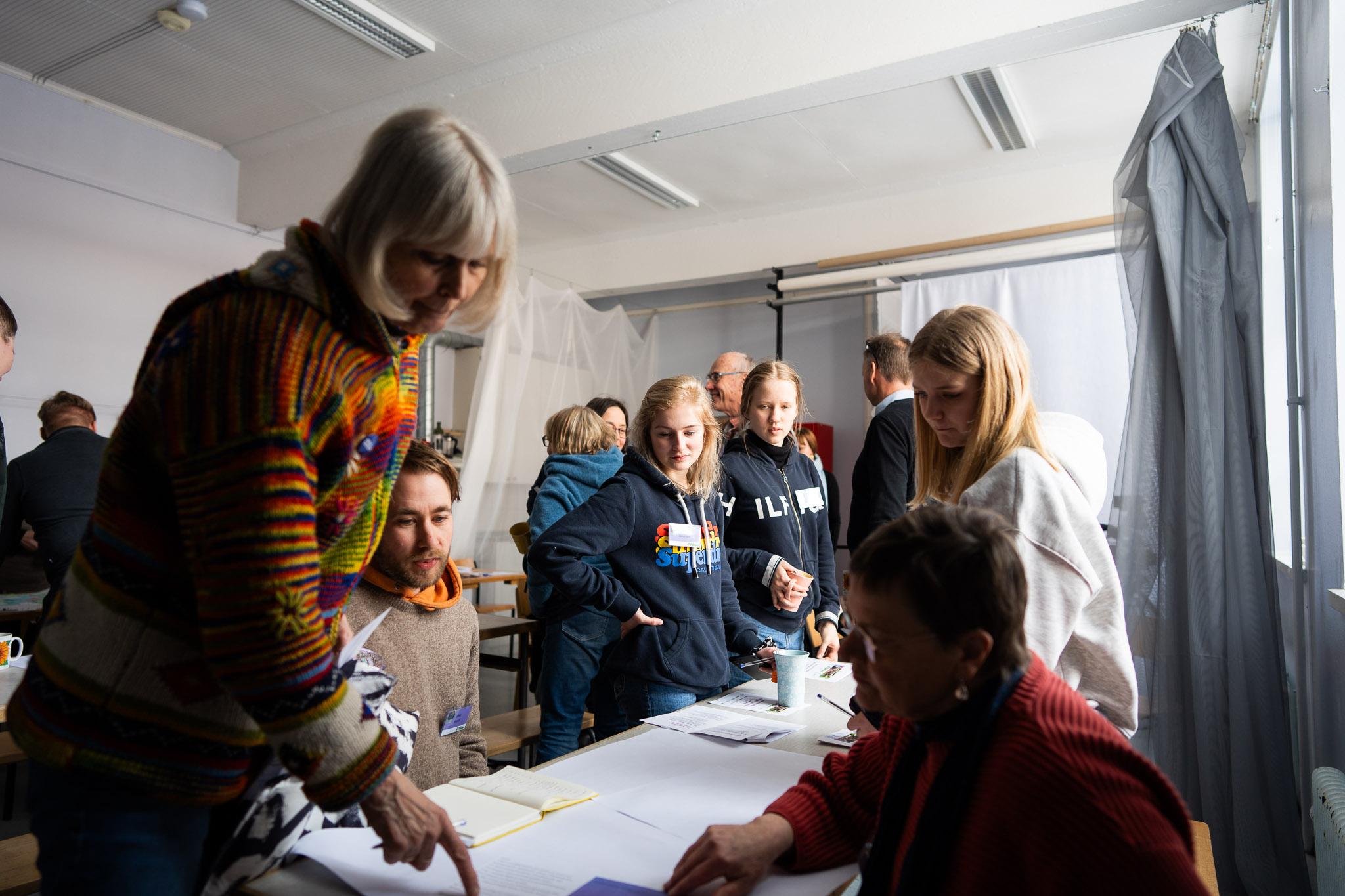 Eri-ikäiset ihmiset osoittavat ja katsovat työpaperia pöydällä.